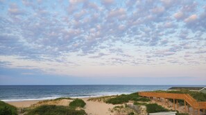 Ein Strand mit einer hölzernen Promenade, die zu einem Gebäude mit grüner Dachbegrünung führt.