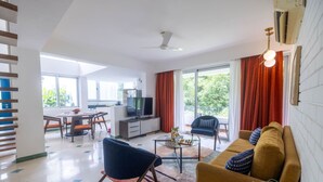 Uma sala de estar moderna com um sofá, uma mesa de centro e uma televisão. Há uma área de jantar com cadeiras e uma mesa.