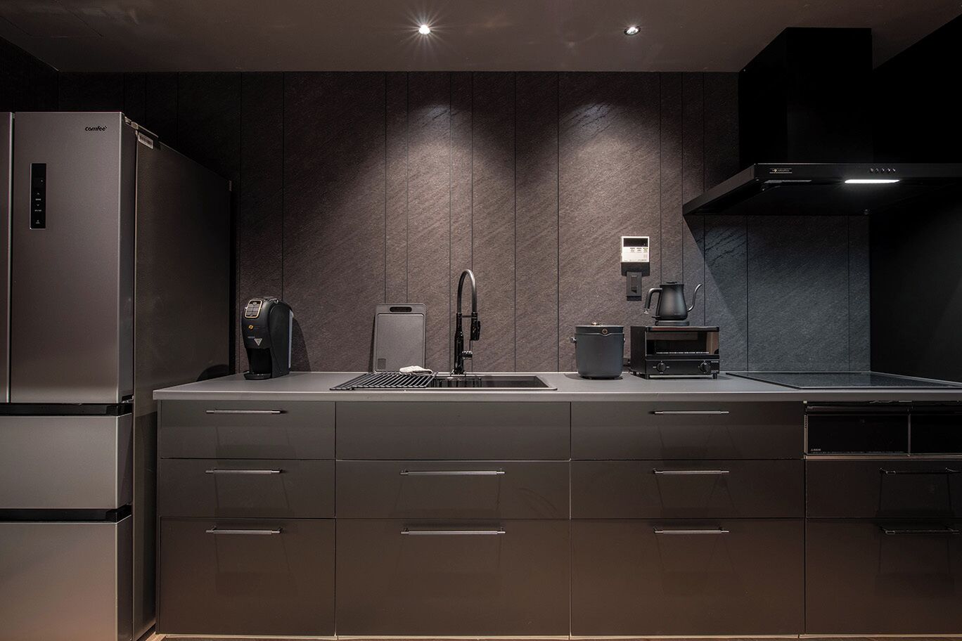 A modern kitchen with a built-in refrigerator, a coffee machine, a kettle, and a stove.