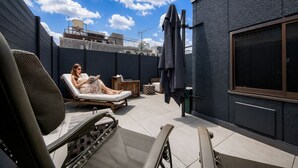 A rooftop terrace with a lounge chair, a person reading, and a view of the cityscape.