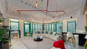 A modern living room with a white sofa, a glass coffee table, and a red chair. There are large windows with a view of the city. - Stunning Open-Concept 3 Bedrooms (Dubai)