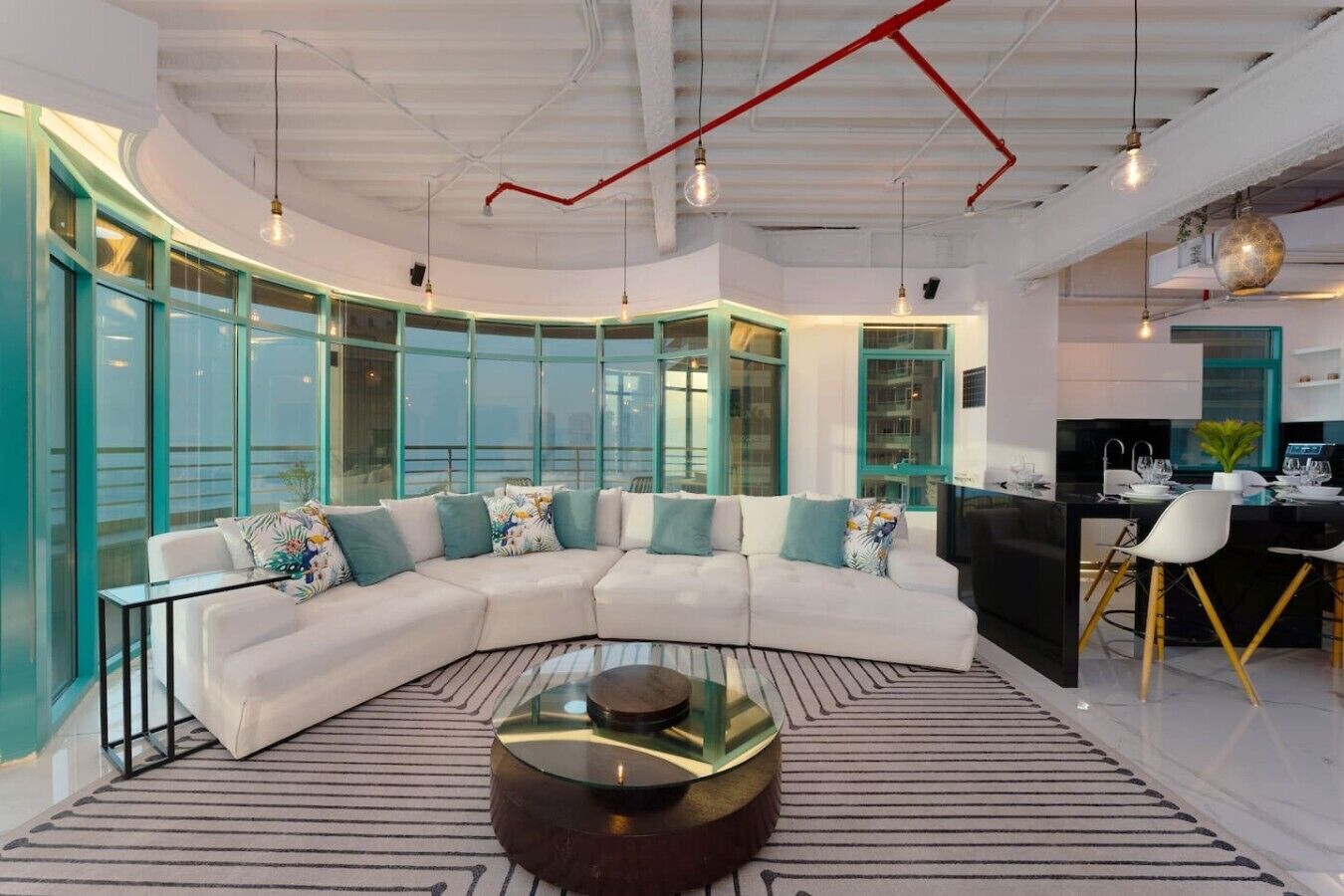 Ein modernes Wohnzimmer mit einem weißen Ecksofa, einem Glastisch und einem Essbereich mit einer schwarzen Kochinsel und weißen Stühlen.
