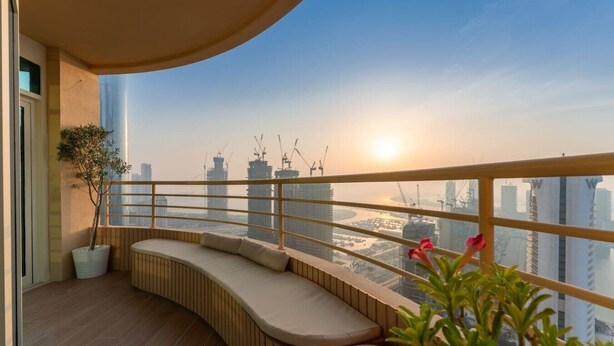 A balcony with a curved seating area, a potted plant, and a view of a cityscape with buildings and a body of water. - Stunning Open-Concept 3 Bedrooms (Dubai)