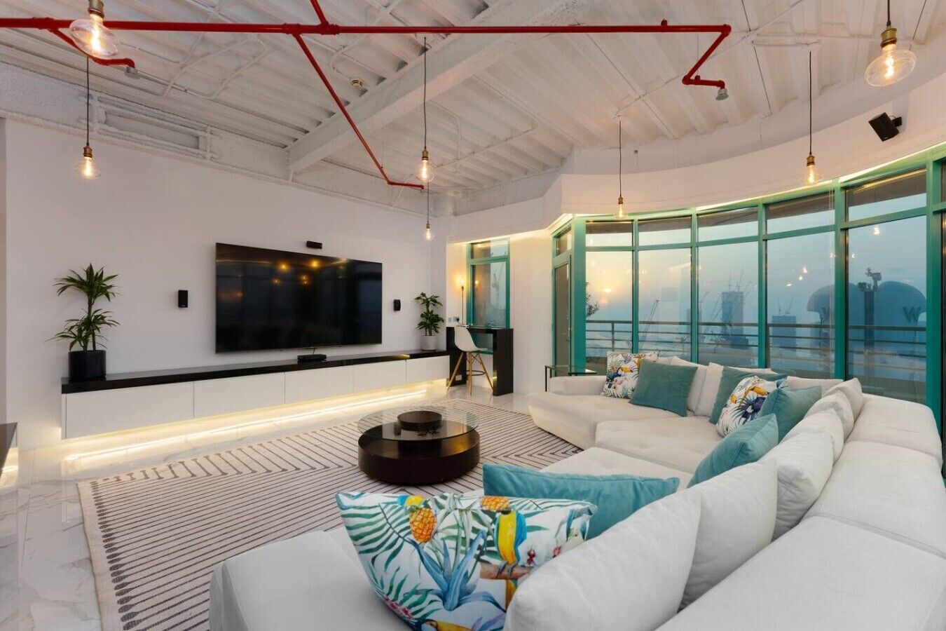 A modern living room with a large flat-screen TV, a round coffee table, and a sofa with colorful cushions.