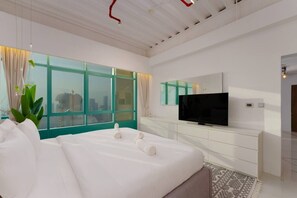 A modern hotel room with a large bed, a flat-screen TV, and a city view through floor-to-ceiling windows. - Stunning Open-Concept 3 Bedrooms (Dubai)