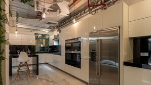A modern kitchen with stainless steel appliances, a marble countertop, and a dining area with a white chair. - Stunning Open-Concept 3 Bedrooms (Dubai)