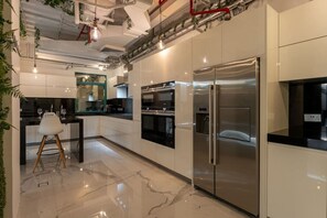 Uma cozinha moderna com eletrodomésticos de aço inoxidável, bancada de mármore e um espaço de refeições com uma cadeira branca.
