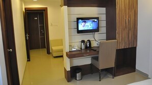 Une chambre d’hôtel équipée d’un téléviseur fixé au mur, d’un bureau avec une chaise, d’une petite poubelle et d’une porte donnant sur une autre pièce.
