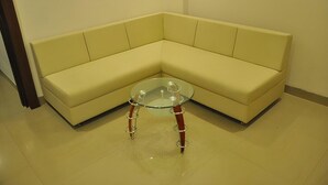 Un canapé d’angle avec une table basse en verre, dans une pièce dont le sol est recouvert de carreaux.