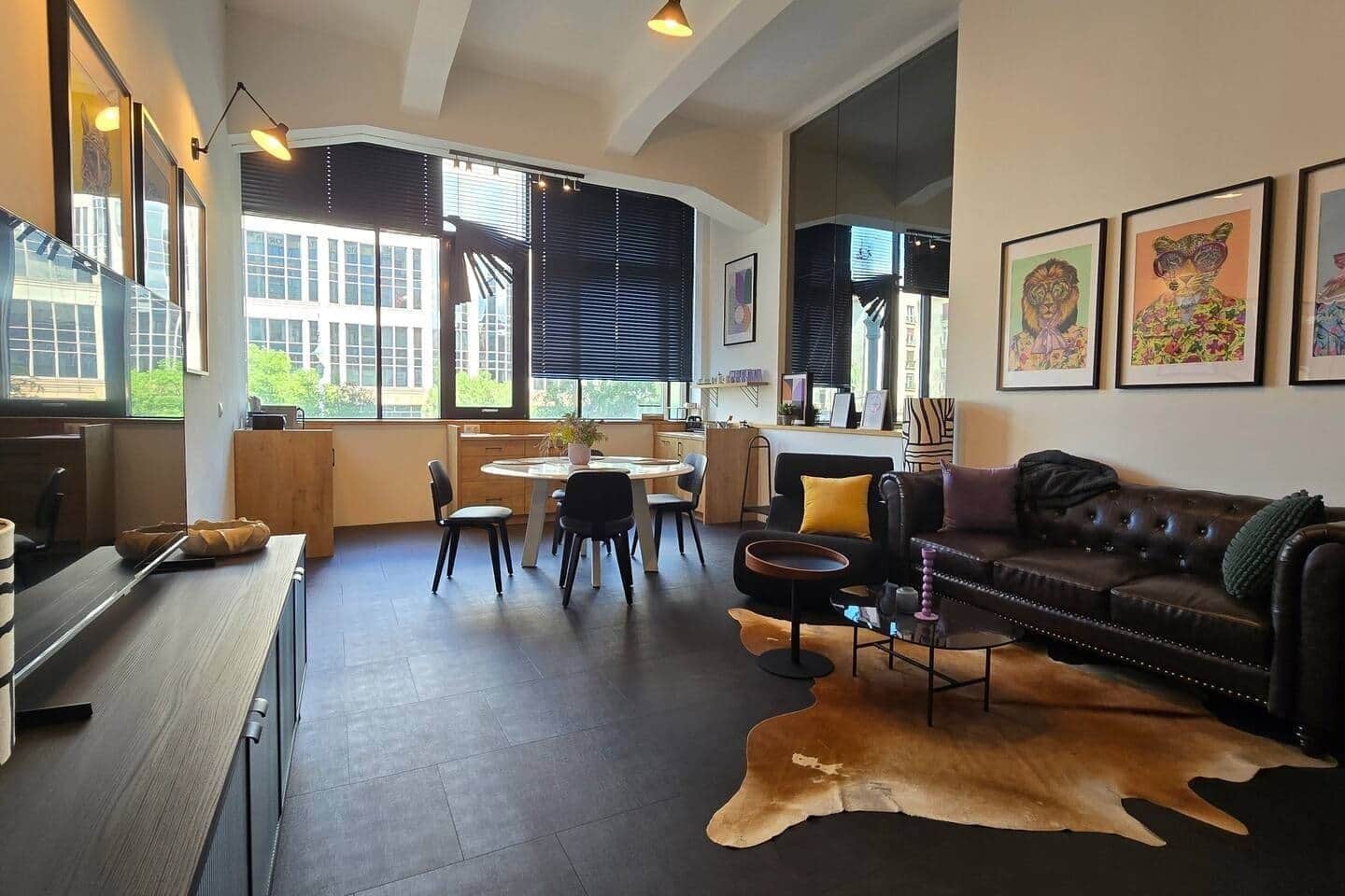A modern living room with a leather sofa, a dining area with a round table, and artwork on the walls.