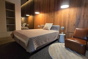 A modern bedroom with a large bed, a chair, and built-in shelving. - IMCT - Astoria Central Home 2 (Budapest)
