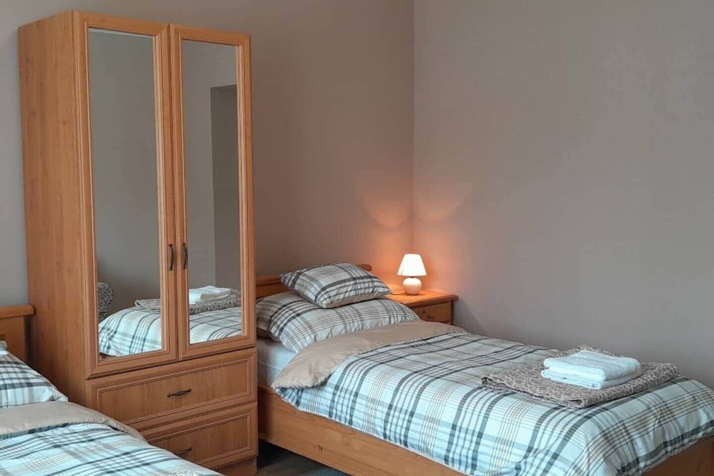 Une chambre avec une armoire en bois, un lit simple avec une couette à carreaux, une lampe de chevet et une petite table.