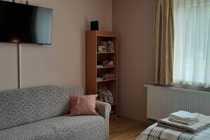 Een woonkamer met een bank, een boekenkast, een radiator en een raam met gordijnen.