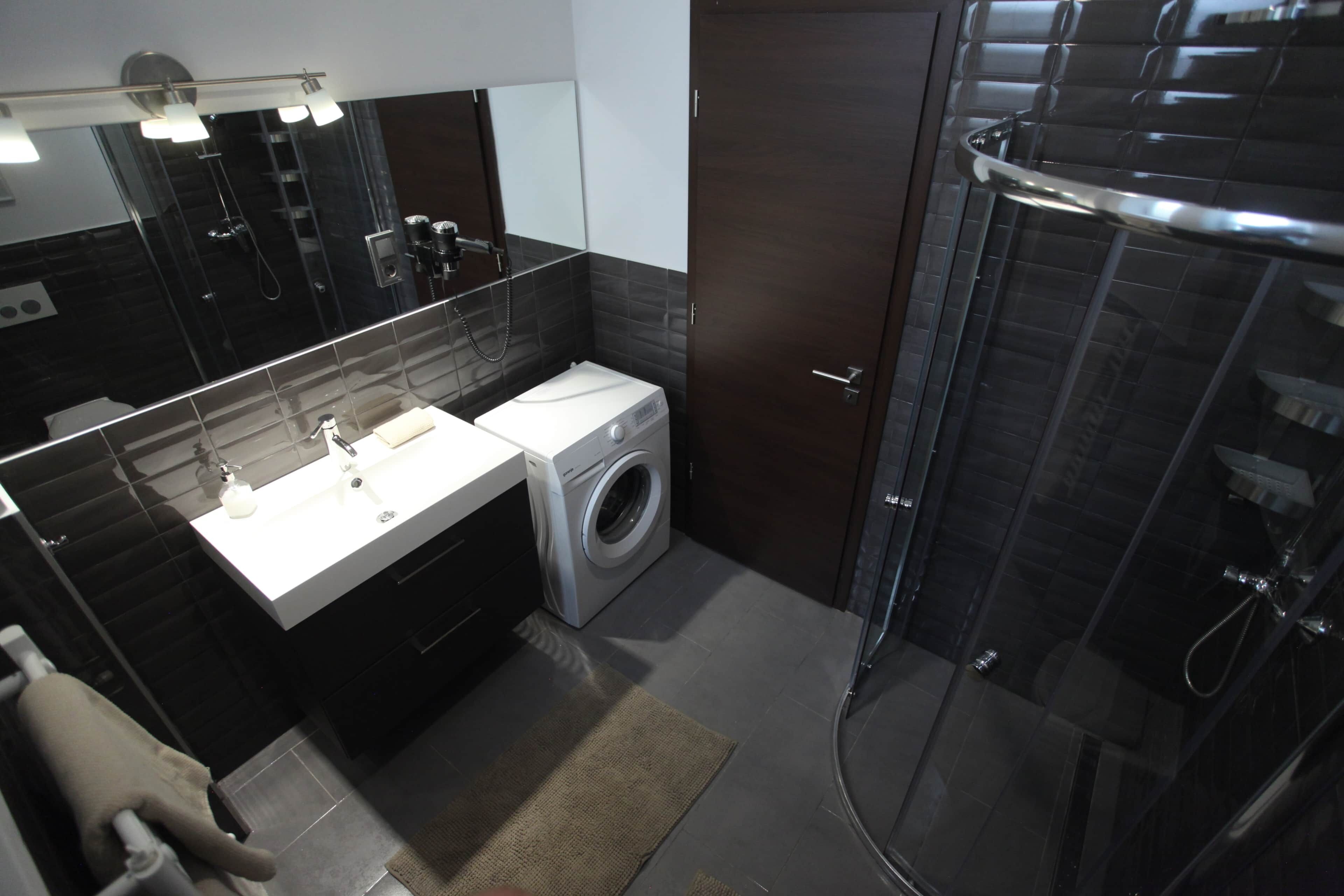 A modern bathroom with a built-in washing machine, a glass shower enclosure, and a large mirror above the sink.