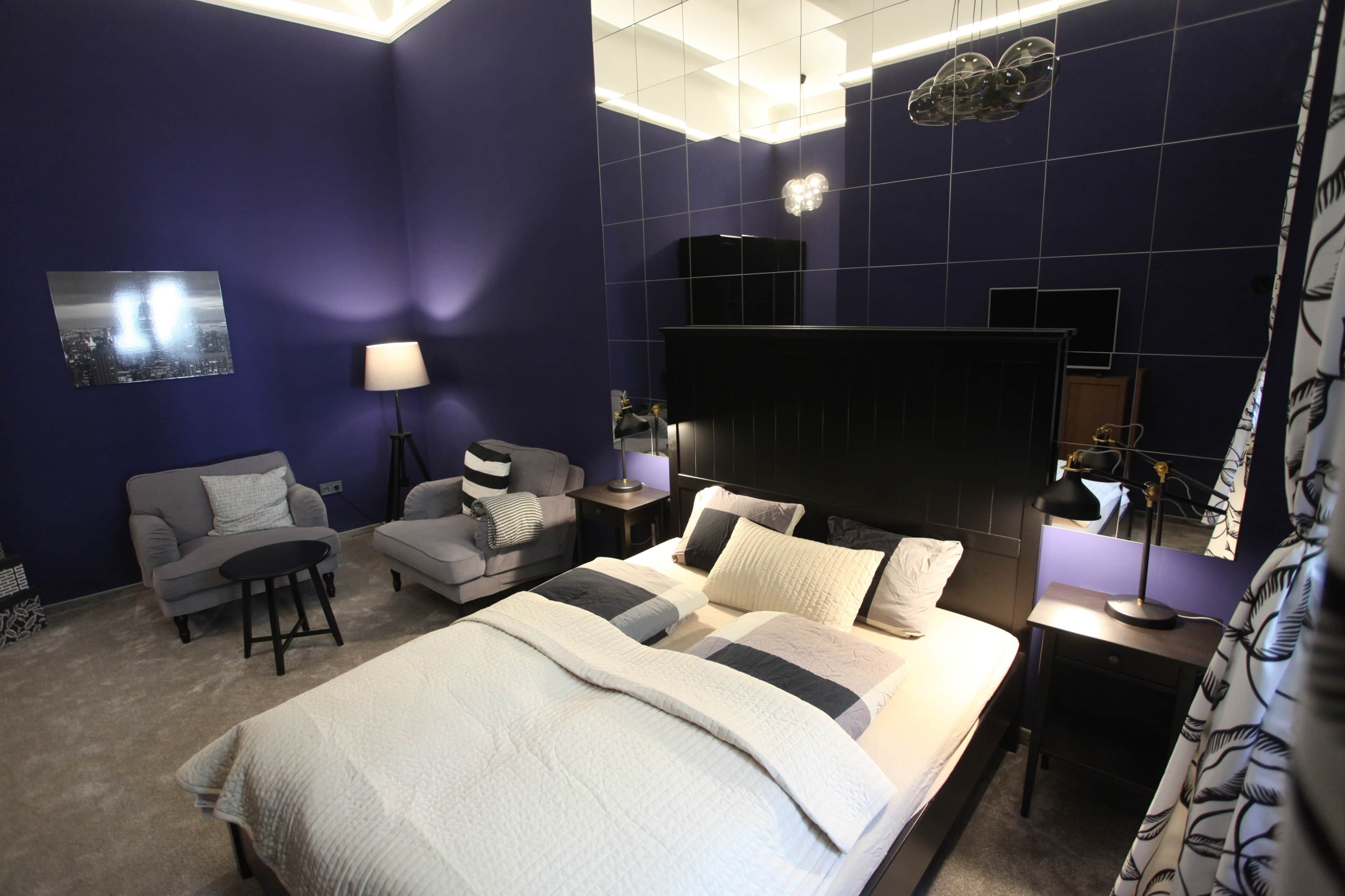 Une chambre à coucher moderne avec un lit, deux canapés, un bureau et un grand miroir.