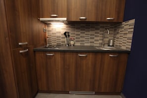 A compact kitchen with wooden cabinets, a stainless steel sink, and a tiled backsplash. - IMCT - Ambassador Apartment (Budapest)
