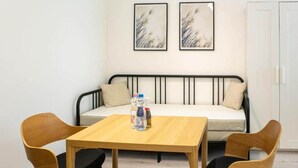 Um quarto pequeno com uma cama, uma mesa com cadeiras e duas molduras na parede.