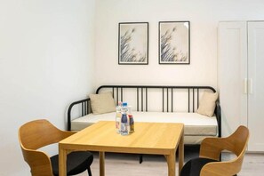 A small room with a bed, a table with chairs, and two framed pictures on the wall. - MidTerm - Rózsa Apartments - Jeremy B (Budapest)