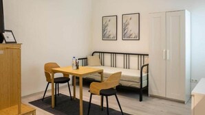 Um quarto com uma cama, uma mesa com cadeiras, uma televisão e obras de arte na parede.