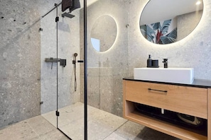 A modern bathroom with a glass-enclosed shower, a round mirror, and a wooden vanity with a white sink. - IMCT - Urban Jungle Apartments 01 (Budapest)