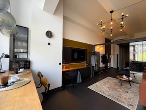 A modern interior with a kitchen area, a dining table with placemats, a seating area with a rug, and a large window. - IMCT - Astoria Central Home 1 (Budapest)