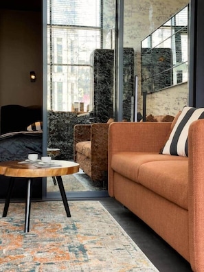 A modern interior with a sofa, a round table, and a large window. - IMCT - Astoria Central Home 1 (Budapest)