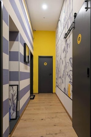 A hallway with striped walls, a yellow accent wall, and a door with a circular emblem. - Dockhouse Soho 4 (Budapest)
