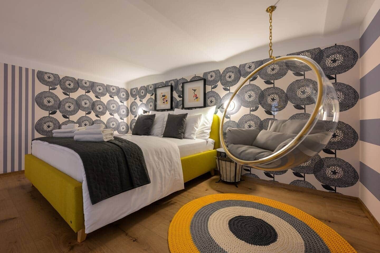 Una camera da letto moderna con un letto, una sedia sospesa e una parete decorata con motivi.