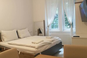 Hotellihuone, jossa on sänky, yöpöytä, tuoli ja ikkuna, jossa on verhot.