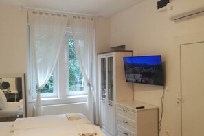 A hotel room with a bed, a TV mounted on the wall, a wardrobe, and a window with curtains. - IMCT - Beliz Apartment 2 in the City Center (Budapest)