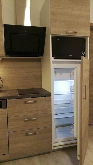 Kompakti keittiö, jossa on mikroaaltouuni jääkaapin yläpuolella, pieni työtaso ja puiset kaapit.