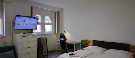A hotel room with a bed, a desk, a chair, a television, and a window.