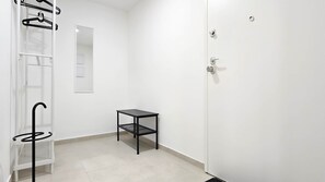 A room with a white door, a black metal shelf unit, and a small black table. - Central Vibe Apartments 1 (Budapest)