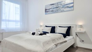 Een hotelkamer met een bed, witte gordijnen, een schilderij en nachtlampjes.