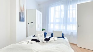A bedroom with a bed, a bedside table, a lamp, and a window with sheer curtains. - Central Vibe Apartments 1 (Budapest)