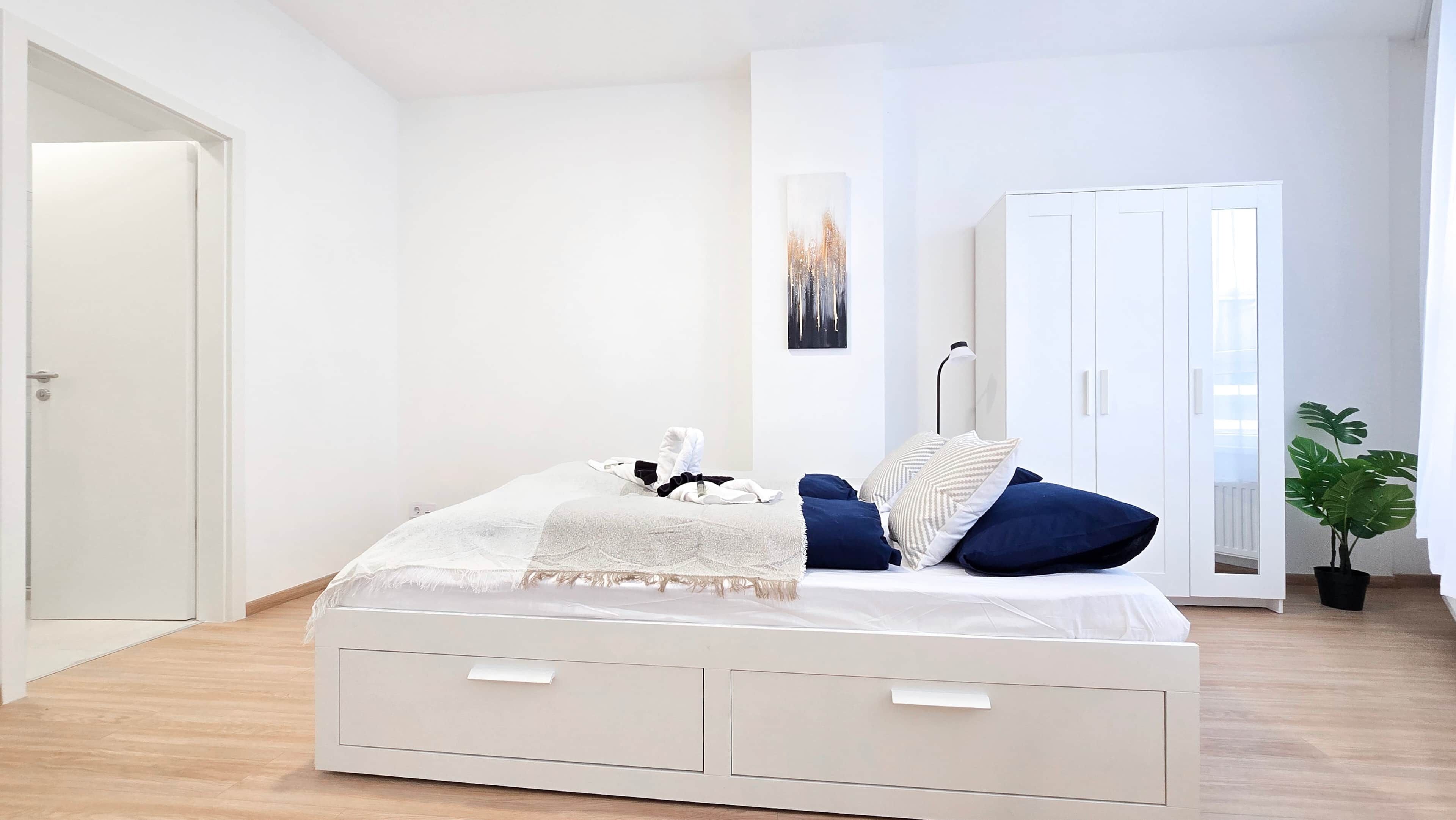 Un dormitorio minimalista con una cama, mesitas de noche, un armario y una planta en maceta.