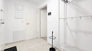 A modern, minimalist room with a white door, a coat rack, and a small shelf. - Central Vibe Apartments 1 (Budapest)