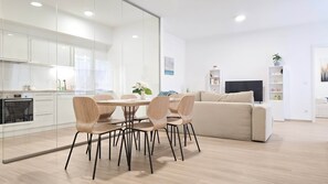 A modern kitchen with white cabinets and a Bosch oven, a dining area with a wooden table and chairs, a beige sofa, and a TV in the living room. - Central Vibe Apartments 1 (Budapest)