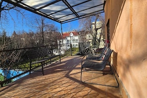 A covered outdoor area with a pool, lounge chairs, and a view of a building with a red roof. - IMCT - City Park Gallery Budapest (Budapest)