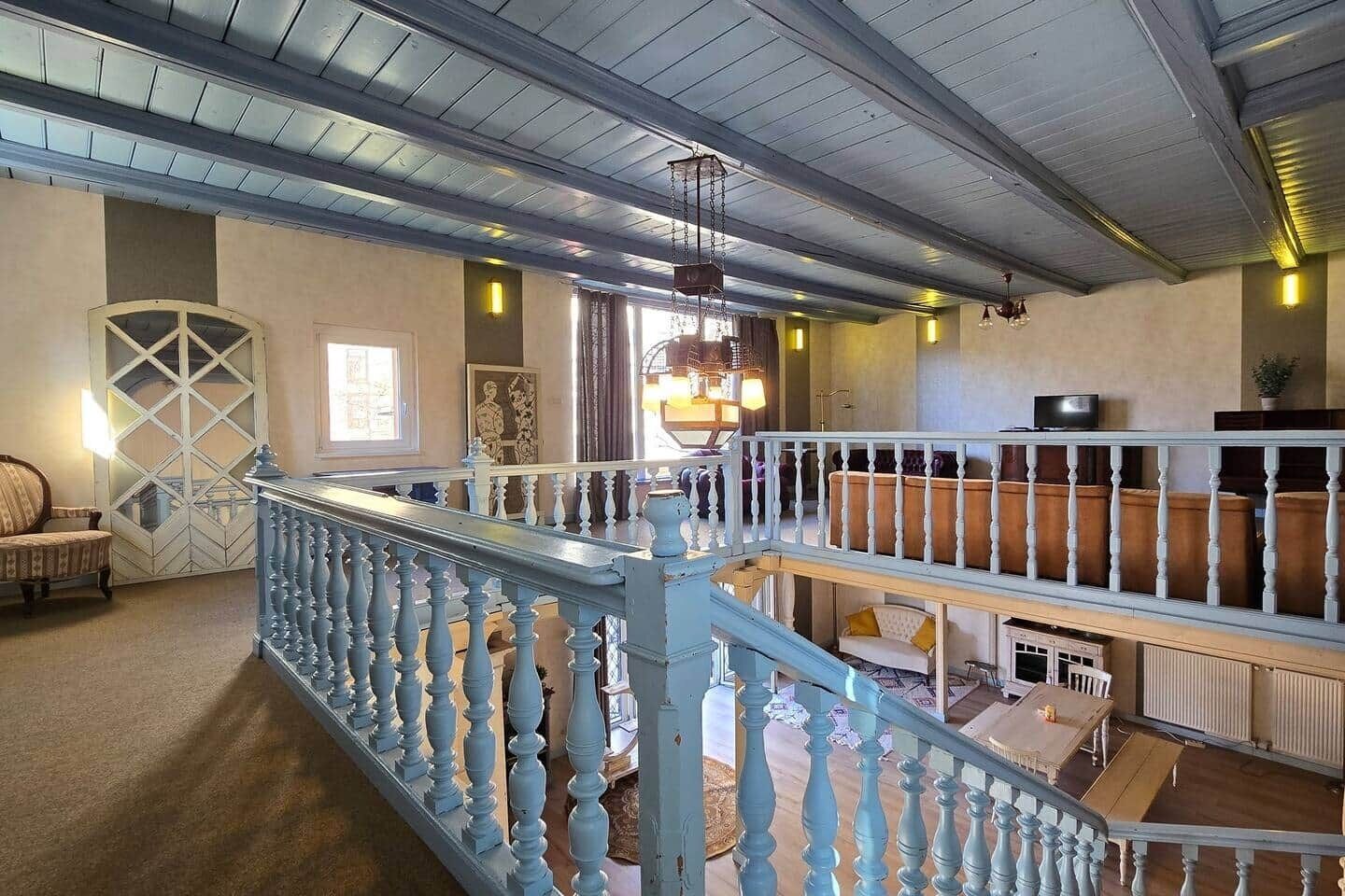 A spacious interior with a high ceiling, a staircase with blue balusters, and a seating area with cushioned sofas.