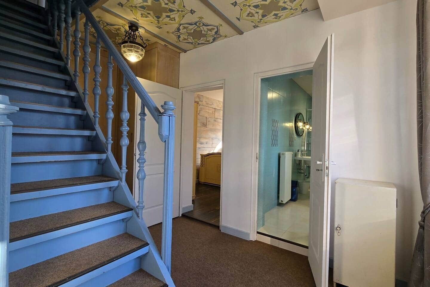 A staircase with a light blue finish, leading to a room with a white door and a bathroom visible through a glass partition.