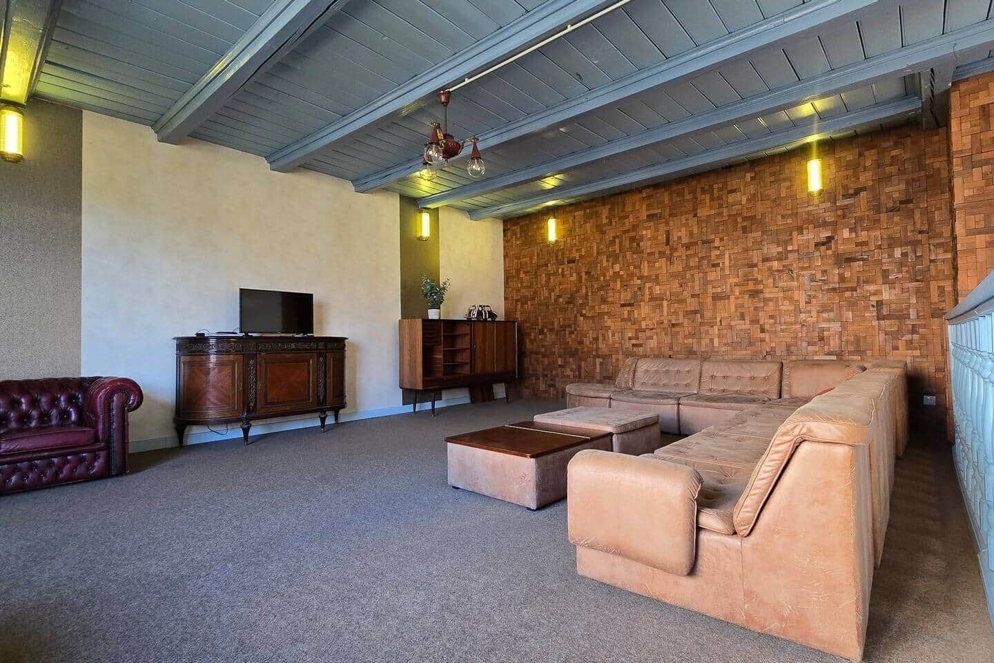 A living room with a sectional sofa, a red leather couch, a wooden entertainment unit, and a brick-patterned wall.