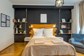 A bedroom with a bed, bedside tables, a nightstand, a chair, and wall-mounted shelves with books and decorative items. - IMCT - d.Five Inspire Apartment Budapest (Budapest)