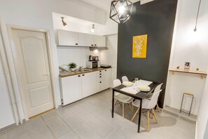 A modern kitchen with white cabinets, a dining table set for four, and a black accent wall with a decorative piece. - IMCT - d.Five Inspire Apartment Budapest (Budapest)