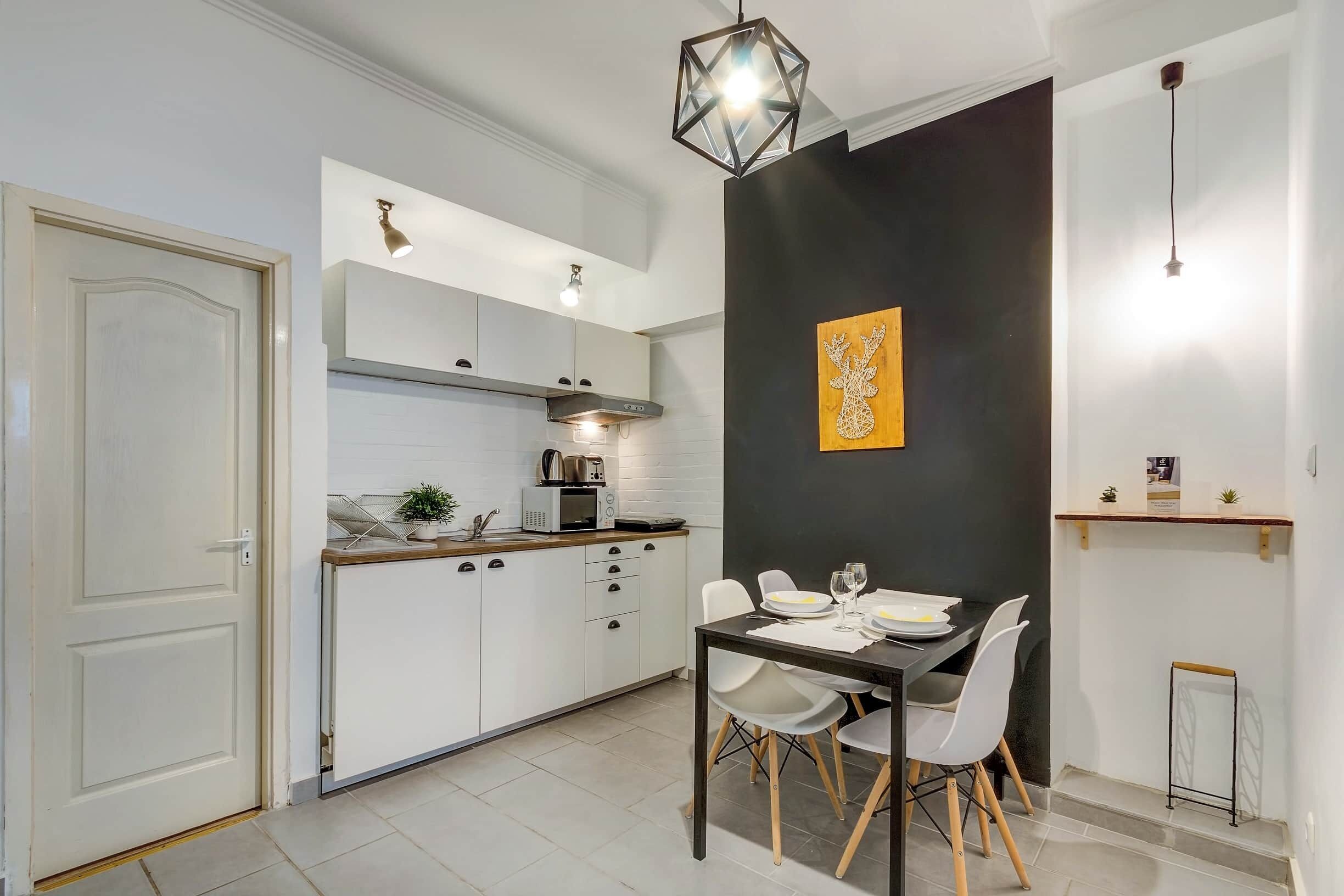 Une cuisine moderne avec des meubles blancs, une table à manger avec des chaises et un mur d’accent noir agrémenté d’un élément décoratif.