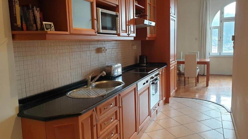 A kitchen with wooden cabinets, a black countertop, a sink, a microwave, and a window with a view.