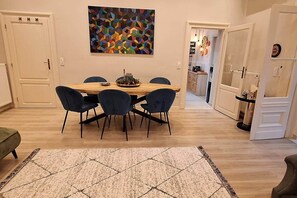 Ein Essbereich mit einem Holztisch, dunklen Stühlen, einem Teppich und einem farbenfrohen, abstrakten Gemälde an der Wand.