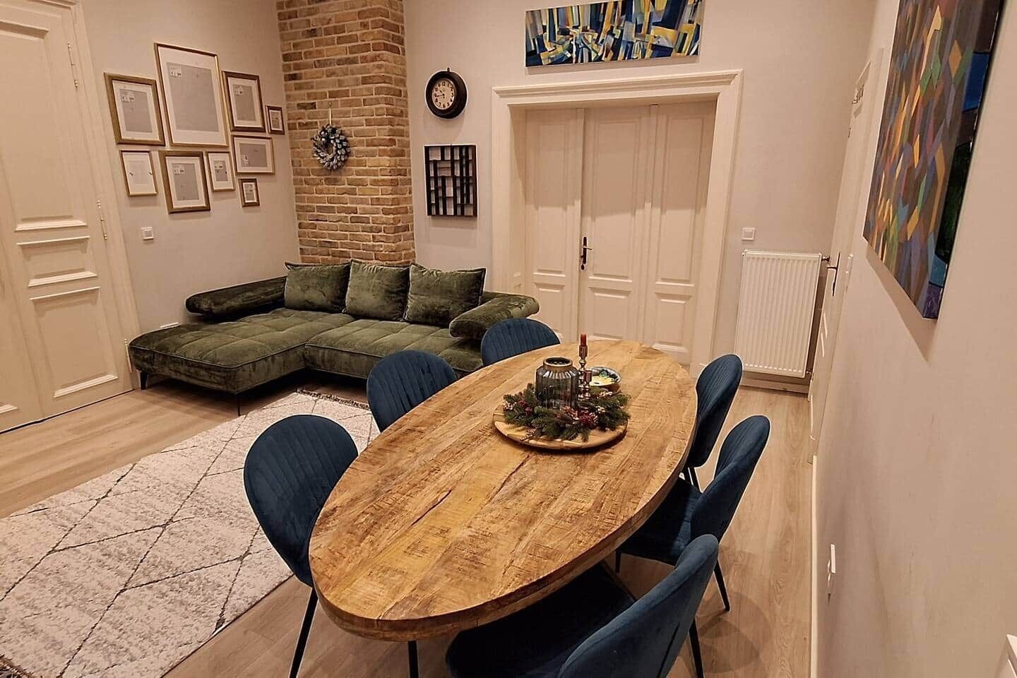 Een eetgedeelte met een houten tafel, blauwe stoelen, een groene hoekbank en een open haard.