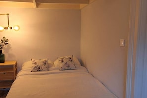 Ein Einzelbett mit Blumenkissen, ein Nachttisch mit einer Vase und eine an der Wand befestigte Lampe.