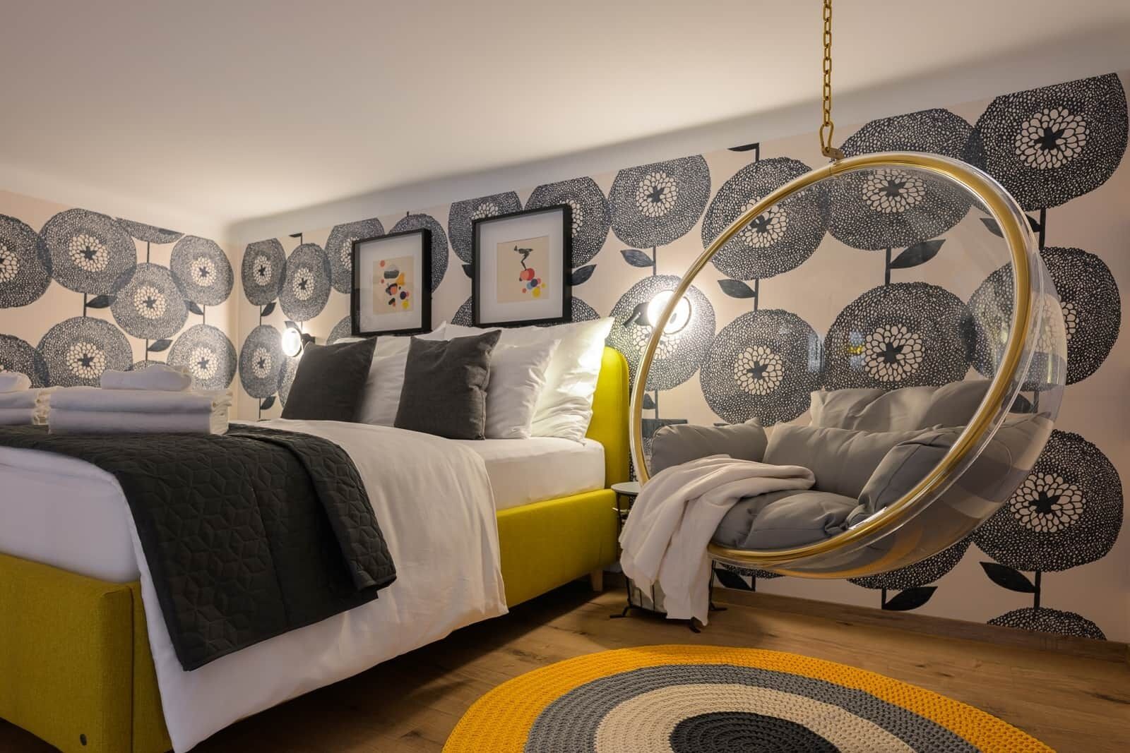 A modern bedroom with a hanging chair, a bed with a yellow headboard, and a wall with a circular pattern.